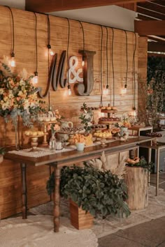 a wooden table topped with lots of food next to a wall covered in hanging lights