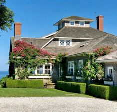 a large house with lots of flowers growing on it's windows and bushes in the front yard