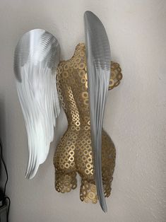 an angel statue with two wings hanging from it's side, against a white wall