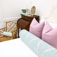 a white bed with pink and blue pillows on top of it next to a dresser