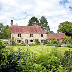 an old house surrounded by lush green grass and flowers in the foreground is a garden