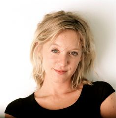 a woman with blonde hair and blue eyes posing for a photo in front of a white wall