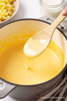 a wooden spoon is being used to stir macaroni and cheese in a pot