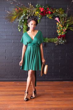 a woman standing in front of a wreath wearing a green dress and holding a hat