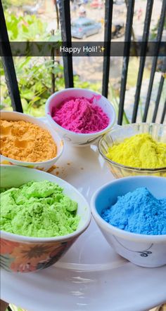 bowls filled with different colored powders on top of a white table next to a window