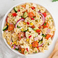 a white bowl filled with pasta salad next to a wooden utensil on top of a table