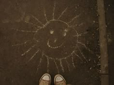 someone's feet are standing in front of a sun drawing on the ground with chalk