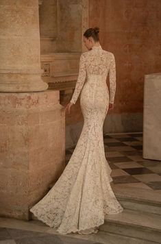 a woman in a long sleeved wedding dress standing next to a pillar and columns