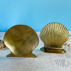 two brass seashells sitting on top of a white table next to each other