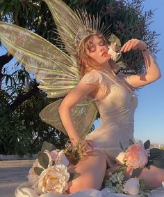 a woman dressed as a fairy sitting on the ground with flowers in her hair and wings