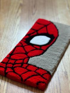 a red and gray rug with a spiderman face on the front is laying on a wooden floor