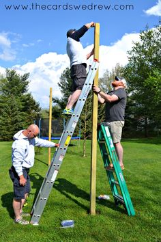 two men are working on a ladder in the grass while another man is standing next to them