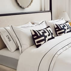 a bed with white and black pillows on top of it next to a wall mounted mirror