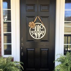 a black front door with a welcome sign on it's side and plants in the foreground