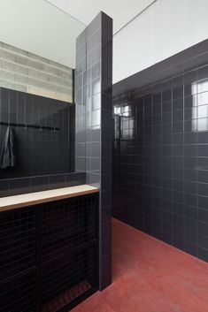 an empty bathroom with black tile walls and red flooring in the shower stall area