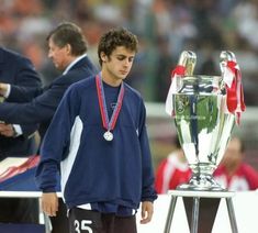 a young man standing next to a trophy on top of a soccer field in front of an audience