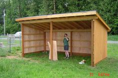 a man standing in front of a wooden shed on top of a grass covered field