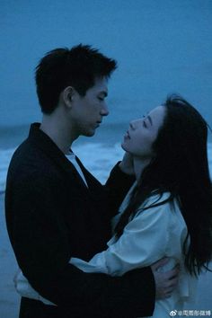 a man and woman standing next to each other on the beach at night with their arms around each other