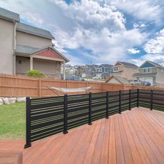 a wooden deck with black iron railings next to a fenced in backyard area