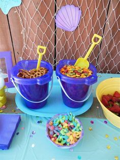 two blue buckets filled with cereal sitting on top of a table next to a bowl of strawberries