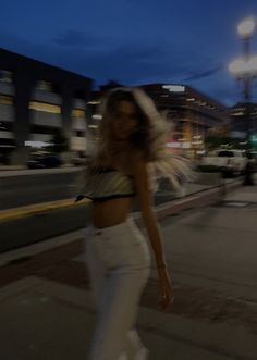 a woman walking down the street at night with her hair blowing in the wind,