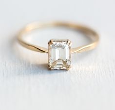 an emerald - cut diamond ring sits on a white surface