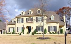 a large white house with lots of windows and trees in front of it on a cloudy day