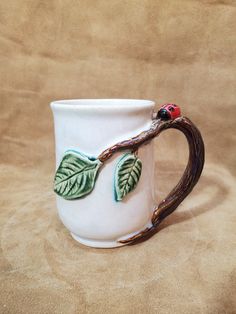 a white coffee mug with green leaves and a ladybug on the handle, sitting on a brown surface