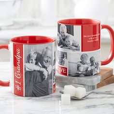 two red coffee mugs sitting on top of a counter next to marshmallows