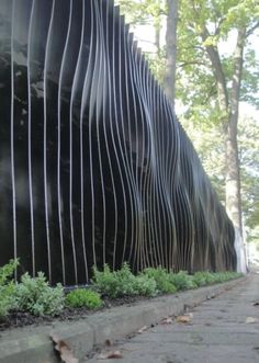 a large metal sculpture sitting on the side of a road in front of trees and bushes