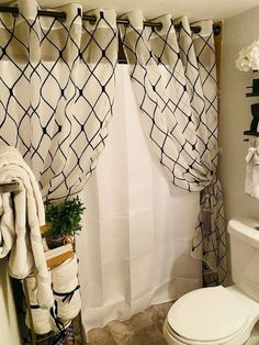 a white toilet sitting next to a bathroom sink under a window covered in black and white curtains