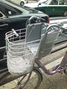 a bike with a basket on the front parked next to a fence and cars behind it