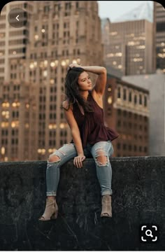 a woman sitting on the edge of a wall in front of a cityscape