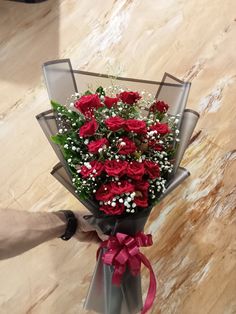 a person holding a bouquet of red roses in their hand on a marble floored surface