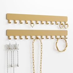 three pairs of gold jewelry hangers on a white wall with chains and rings hanging from them