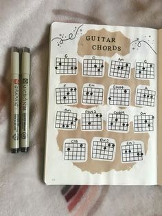 an open notebook with guitar chords on it next to two markers and one marker pen