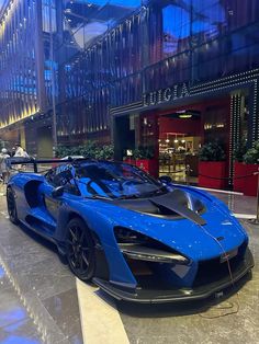 a blue and black sports car parked in front of a building with people walking by