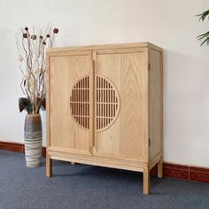 a wooden cabinet sitting next to a vase with dried flowers in it on the floor