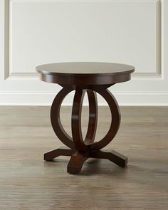 a round wooden table sitting on top of a hard wood floor next to a white wall