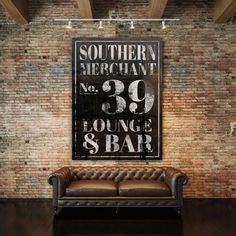 a leather couch sitting in front of a brick wall with an old sign on it