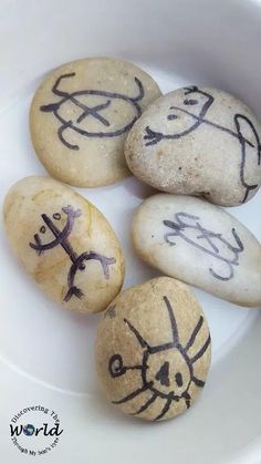 four rocks with drawings on them sitting in a bowl