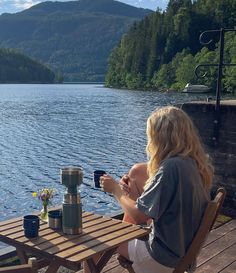 a woman sitting at a wooden table next to a lake