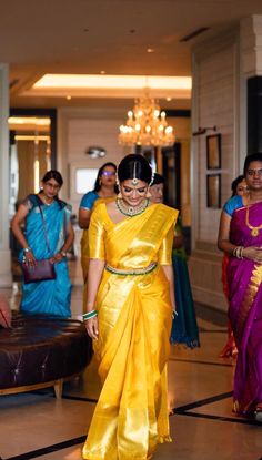 a woman in a yellow sari walking down the hall with other people behind her