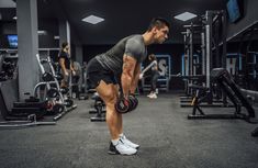 a man is doing squats with dumbbells in the gym while other people are working out behind him