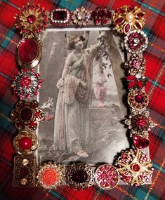 an old fashion picture frame with red and gold brooches on the edges, sitting on a plaid table cloth