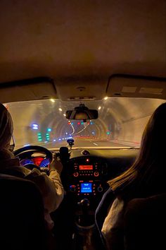 two people in a car driving through a tunnel at night with lights on the ceiling