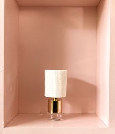 a pink shelf with a white lamp on top and a gold base in the corner