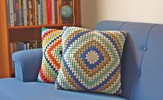 a blue couch with two crocheted pillows on it in front of a bookshelf