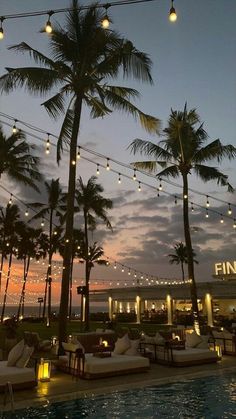 an outdoor swimming pool with lounge chairs and palm trees at sunset in front of the finola hotel