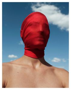 a man wearing a red cloth covering his face and neck in front of a blue sky with clouds